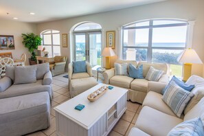 A spacious living room with a large window, a white coffee table, and a seating area with a sofa and chairs.