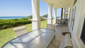 A covered patio with a glass table and chairs, a view of the ocean, and a well-maintained lawn. - Gulf front condo, 1st floor- walk out to beach, Pool, Santa Rosa beach (Santa Rosa Beach)