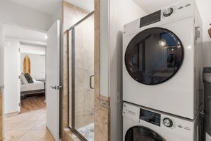 A laundry area with stacked washing machines and a glass shower door. - Exquisite Escape: Elegantly Renovated Wailea Elua 801 – Tranquil Paradise (Wailea, Maui)