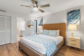 A bedroom with a bed, bedside tables, a ceiling fan, a wall-mounted mirror, and artwork.