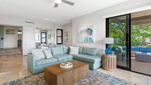 A modern living room with a light blue sofa, a wooden coffee table, and a large window with a view of the outdoors.