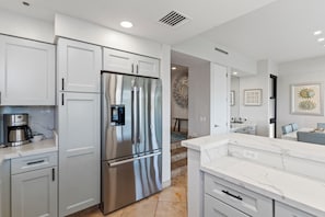 A modern kitchen with white cabinetry, a stainless steel refrigerator, and a marble countertop. - Exquisite Escape: Elegantly Renovated Wailea Elua 801 – Tranquil Paradise (Wailea, Maui)