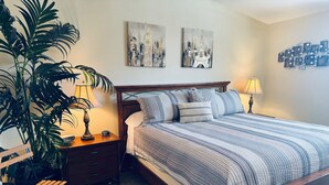 A neatly arranged bedroom with a wooden bed, striped bedding, a nightstand with a lamp, a bedside table, and a large potted plant. - Crow's Nest by Mesquite Vacation Rentals: Stunning Views of Mesquite and $510 in free daily activities (Mesquite)