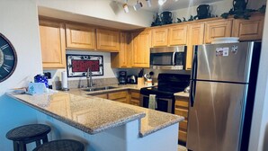 A kitchen with granite countertops, wooden cabinets, stainless steel appliances, and a clock on the wall. - Crow's Nest by Mesquite Vacation Rentals: Stunning Views of Mesquite and $510 in free daily activities (Mesquite)