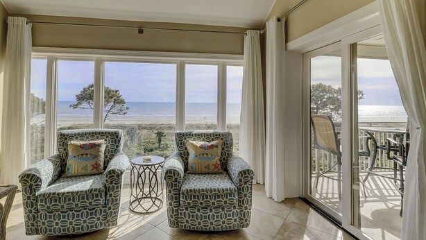 Een balkon met twee gestoffeerde fauteuils en een kleine ronde tafel, met uitzicht op een strand en de oceaan.