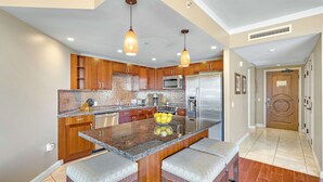 A modern kitchen with wooden cabinets, stainless steel appliances, and a central island with bar stools. - Maui Resort Rentals: Honua Kai Konea 515 - Upgraded 5th Floor Oceanview Studio (Lahaina)