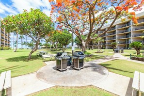 Relax in a serene outdoor space surrounded by lush greenery and trees, featuring a central seating area with barbecue grills.