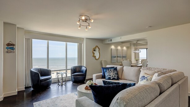 Een ruime woonkamer met een groot raam met uitzicht op de oceaan, een moderne kroonluchter en een eethoek met panoramisch uitzicht.