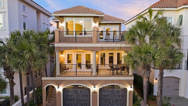 A two-story residential building with a balcony, garage doors, and palm trees. - Casa Lontano - Luxury Home Near the Beach with Gulf Views & Shared Pool (Destin)