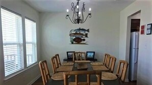 A dining room with a rectangular table, six wooden chairs, a chandelier, and a fish wall decoration. - South Harbor Condo. 3 Bedroom, 3 Bath. Boat Slip. LED Fishing Light. Large Deck. (Port Mansfield)