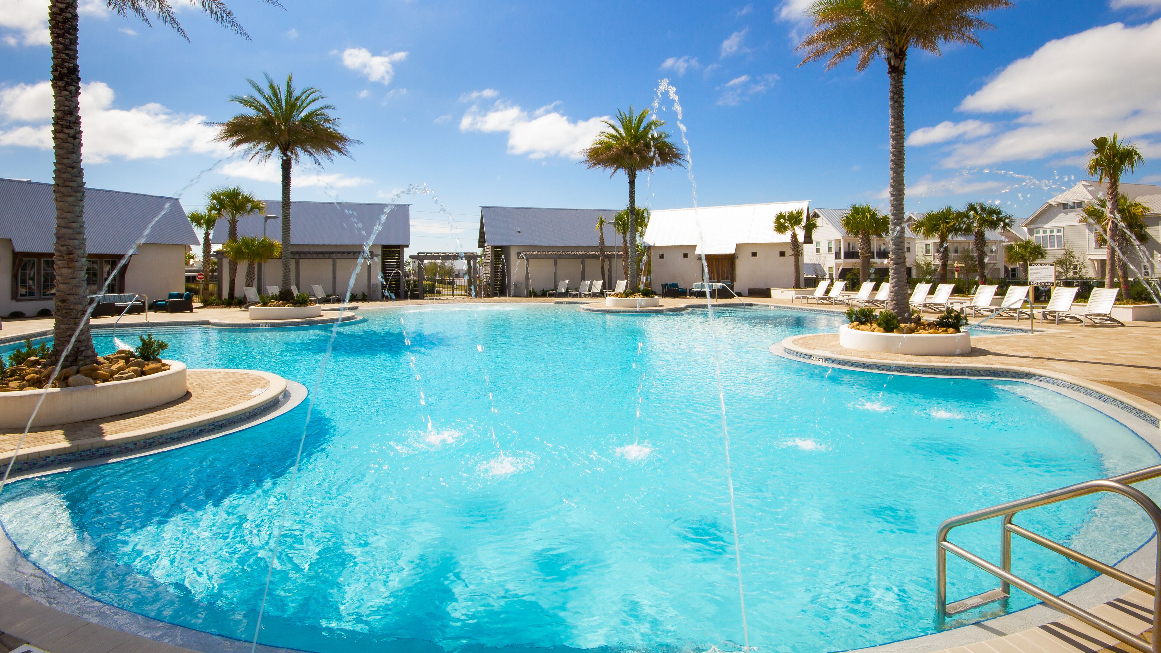 A swimming pool with water fountains, palm trees, and lounge chairs.