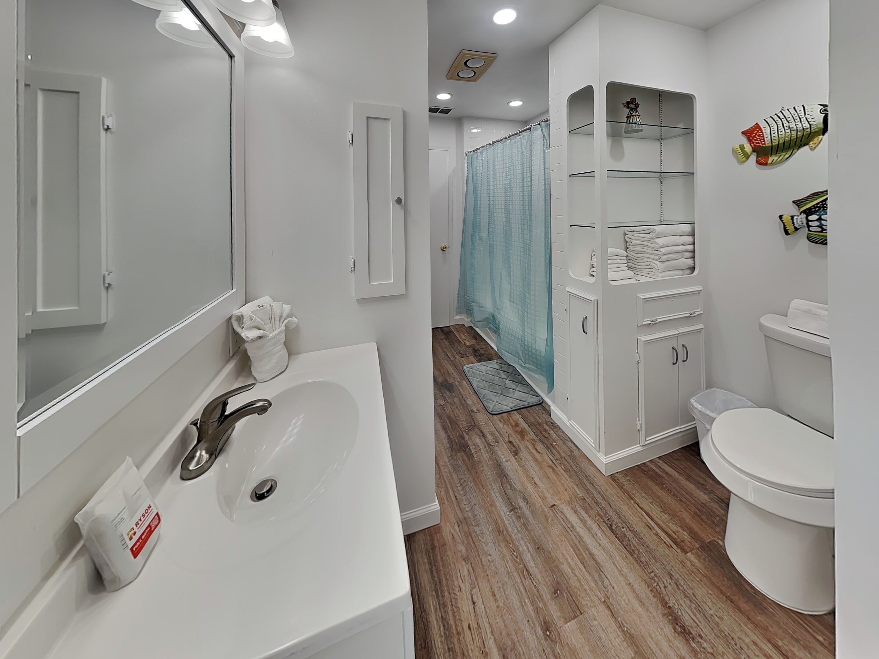 A modern bathroom with a white sink, mirror, and toilet. There are shelves with towels and a shower curtain.