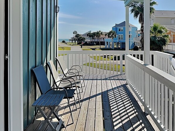 A wooden deck with white railings and a view of a coastal area with buildings and palm trees.