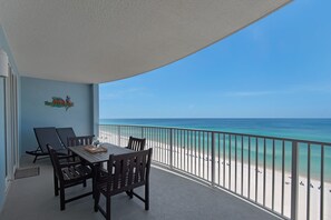 A balcony with a view of the beach, a table with chairs, and a sign with a parrot and palm tree. - GULFFRONT AND GORGEOUS! 10TH FLOOR! SLEEPS 6 (Panama City Beach)