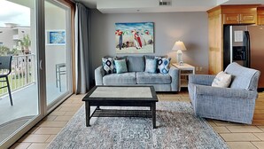 Una sala de estar con sofá, sillón, mesa de centro y un cuadro de sombrillas de playa.