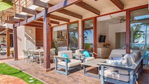 Ein großzügiger Außenbereich mit Holzboden, einer überdachten Terrasse und einer Sitzgruppe am Pool mit Kissen.