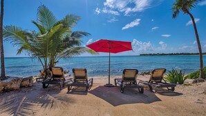 Ein Strand mit vier Liegestühlen, einem roten Sonnenschirm und Palmen.