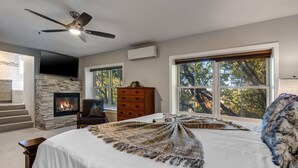 A bedroom with a fireplace, a large bed, a ceiling fan, and a view of trees through a window. - Epic Home Just Steps to Main Street + Hot tub (Park City)