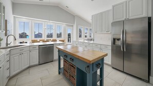 Een moderne keuken met witte kasten, een houten eiland en een roestvrijstalen koelkast.