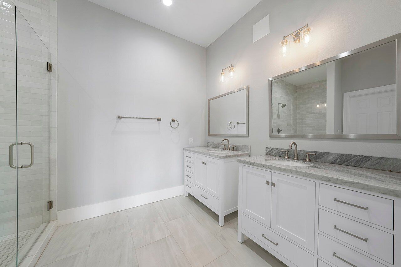 Une salle de bain moderne avec une douche à l’italienne en verre, des meubles blancs et un grand miroir au-dessus du lavabo.