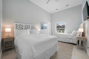 A modern bedroom with a large bed, a smaller bed, a window with a view, and a ceiling fan.
