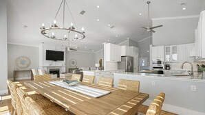 Een moderne keuken met witte kasten, een centraal eiland en een eethoek met een houten tafel en rieten stoelen.