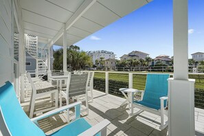 A covered outdoor area with white furniture, including chairs and a table, overlooking a residential area with houses and greenery.