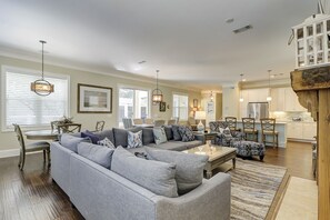 Un salón espacioso con un sofá seccional gris, un comedor con una mesa redonda y una cocina con armarios blancos y una isla de madera.