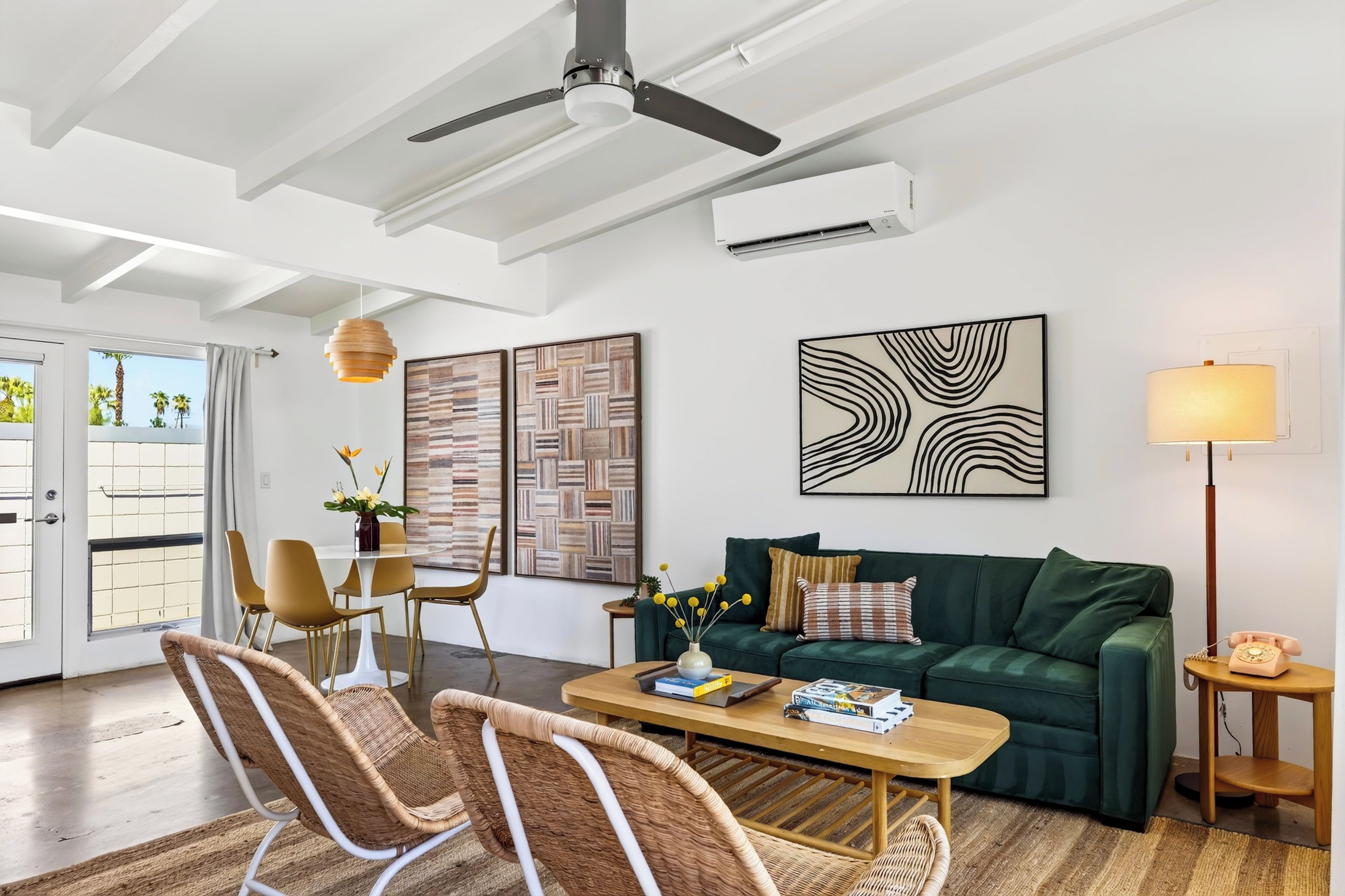 Een moderne woonkamer met een plafondventilator, een groene bank, een eettafel met stoelen en kunstwerken aan de muren.