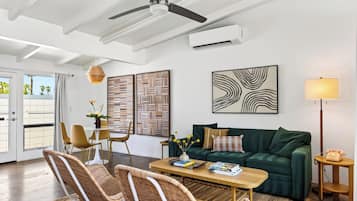 Een moderne woonkamer met een plafondventilator, een groene bank, een eettafel met stoelen en kunstwerken aan de muren.