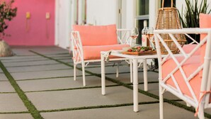 Un espace extérieur aménagé avec des meubles en osier blanc et des coussins orange, un panier en osier et une table sur laquelle se trouvent une bouteille et des verres.