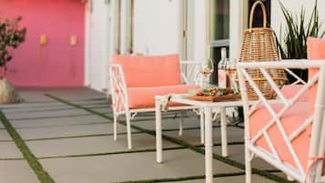 Een terras met witte wicker meubels en oranje kussens, een rieten mand en een tafel met een fles en glazen.