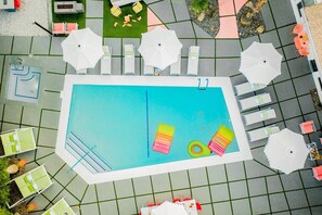 An aerial view of a swimming pool area with lounge chairs, umbrellas, and a poolside bar.