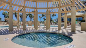Une piscine circulaire surmontée d’une pergola, entourée de chaises longues et de palmiers.