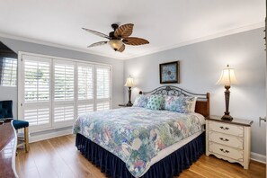 Un dormitorio con una cama, dos lámparas de noche, un ventilador de techo, una ventana con persianas y una silla.