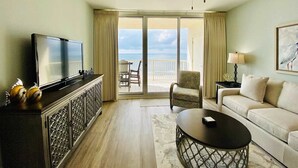 A hotel room with a television, a sofa, a coffee table, a ceiling fan, and a balcony with a view of the sea. - Beach Club 1004B by ALBVR - Beachfront Beauty - New appliances and bunk beds (Gulf Shores)