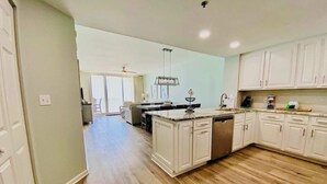 A spacious kitchen with white cabinets, a central island, and a dining area with a ceiling fan. - Beach Club 1004B by ALBVR - Beachfront Beauty - New appliances and bunk beds (Gulf Shores)