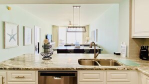 A modern kitchen with white cabinetry, a stainless steel dishwasher, and a central island with a sink. - Beach Club 1004B by ALBVR - Beachfront Beauty - New appliances and bunk beds (Gulf Shores)