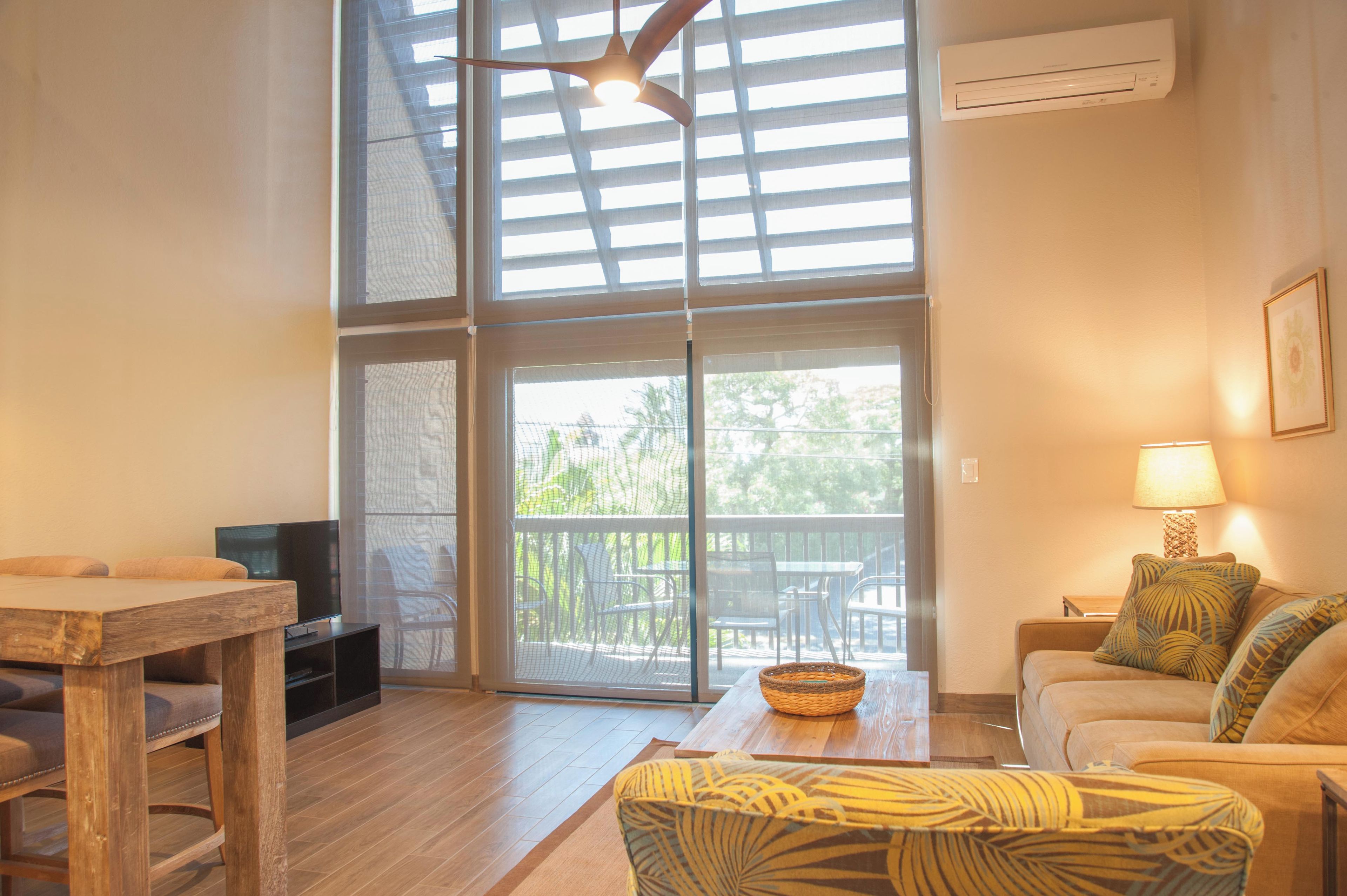 A living room with a TV, wooden furniture, a ceiling fan, and a view through large glass doors to an outdoor patio.
