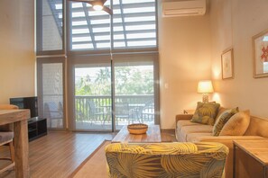 A living room with a sofa, a coffee table, a TV, and a balcony with outdoor furniture.