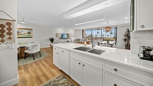A modern kitchen with white cabinetry, a large island with a sink, and a view of the outdoors. - Sundial P301 Vacation Rental on Sanibel Island (Sanibel)