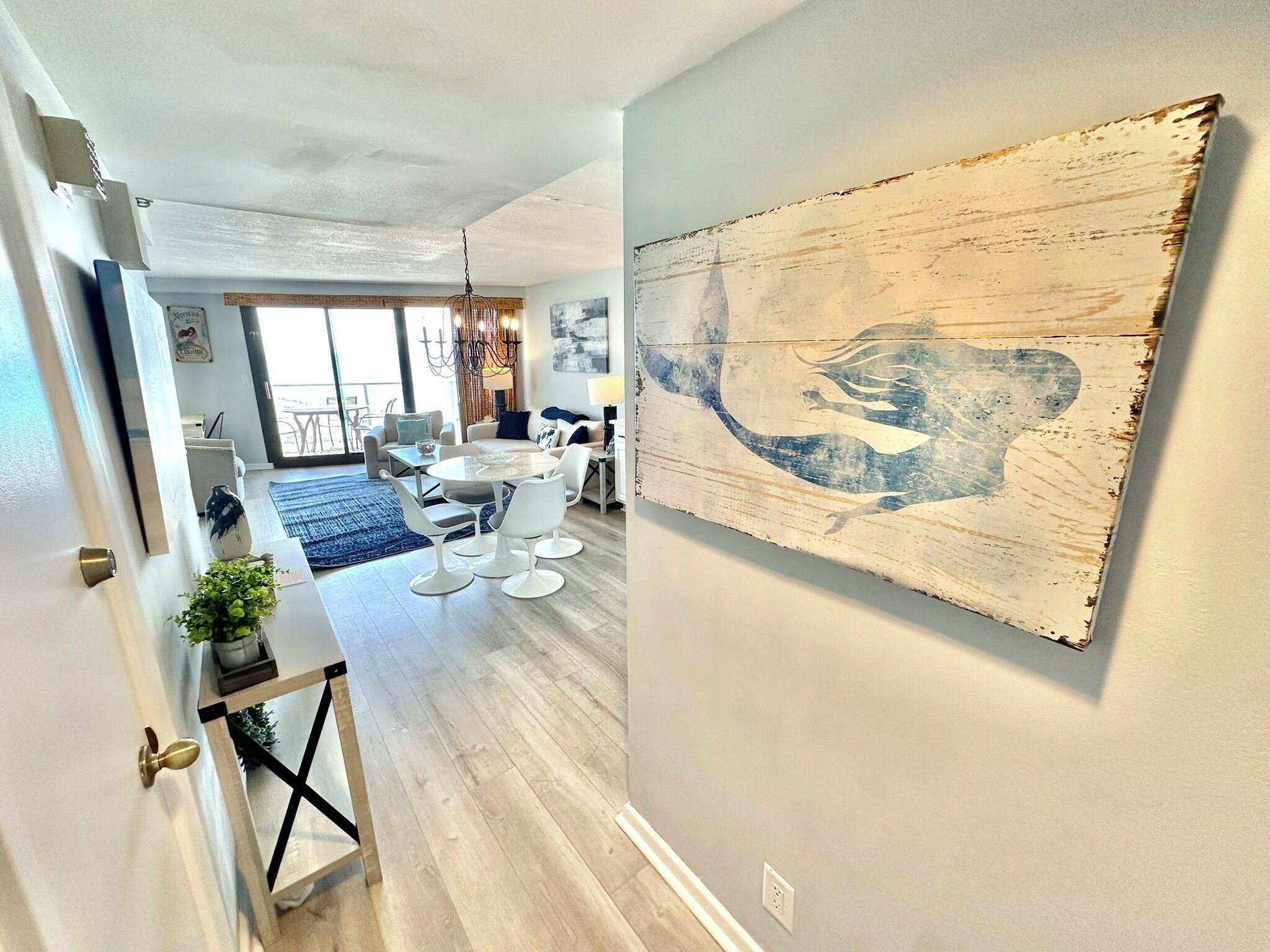 Un salon moderne avec un coin repas, une grande peinture abstraite au mur et une vue sur l’extérieur par la porte ouverte.