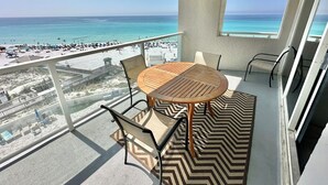 Un balcón con vista a la playa y al océano, una mesa de madera redonda y dos sillas.