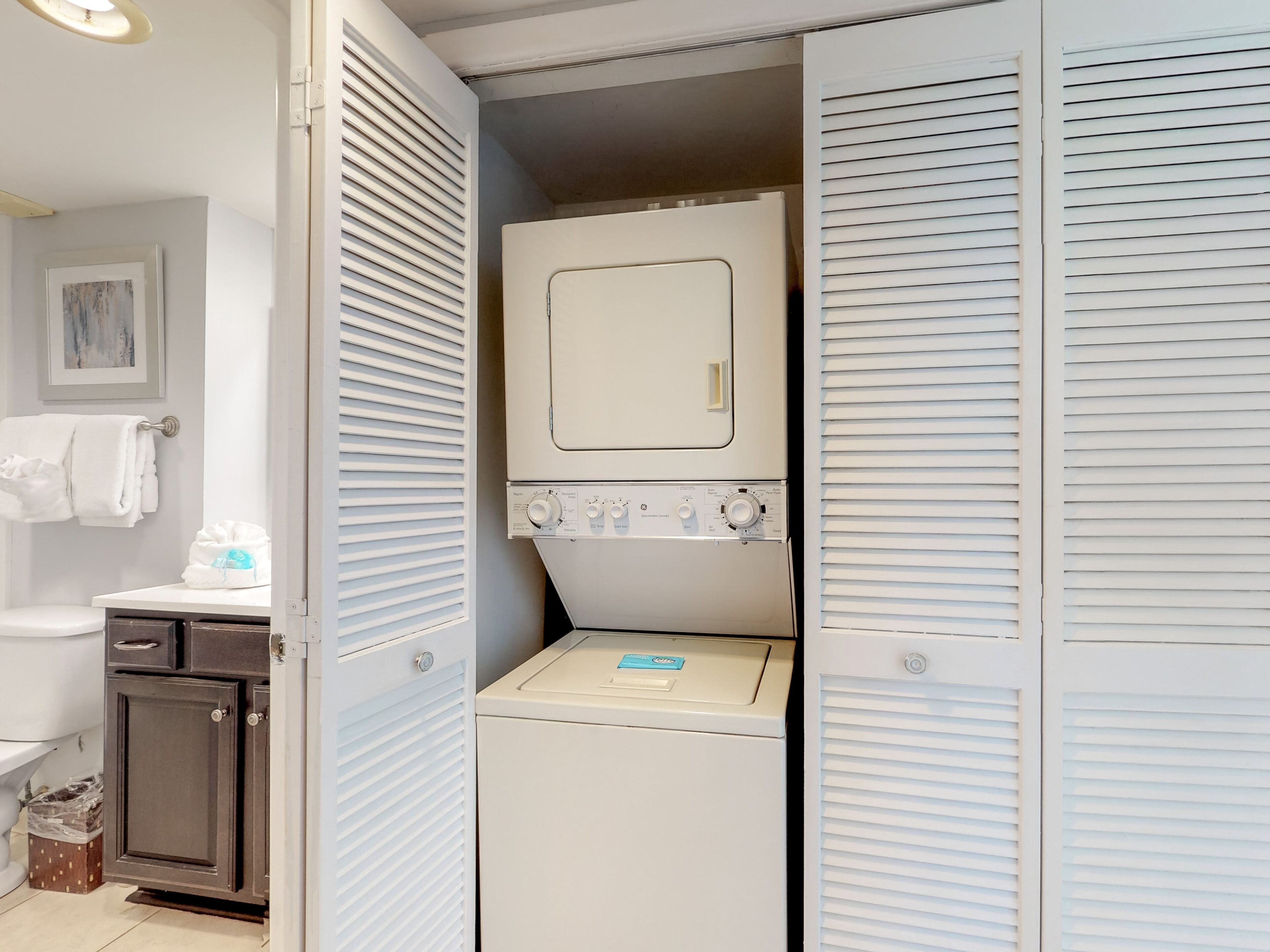 A compact laundry room with a washing machine and dryer, a small cabinet, and a towel rack.