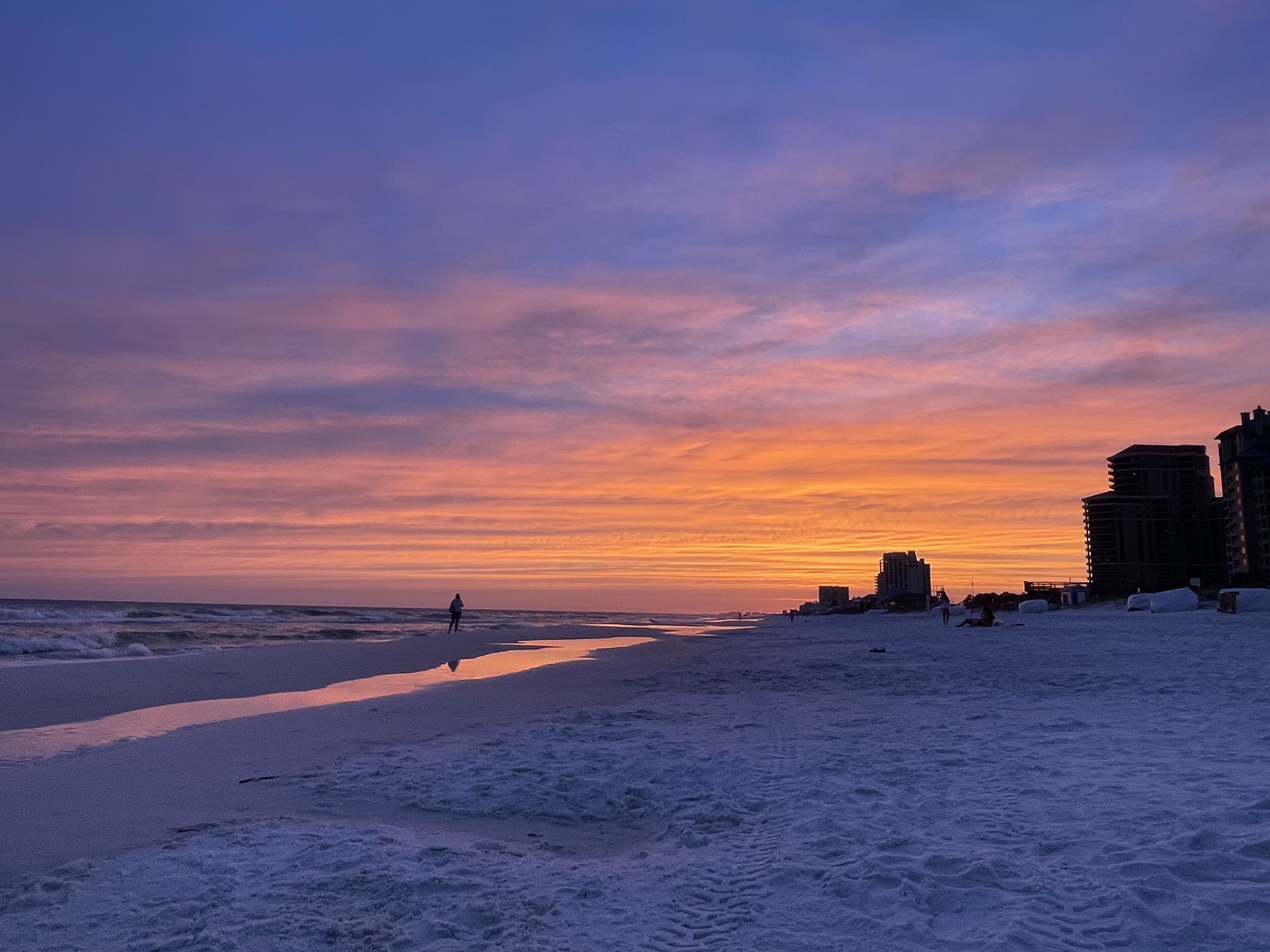 A beach with a sunset, buildings in the background, and footprints on the sand.