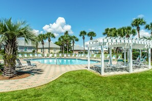 Relax by the pool surrounded by palm trees and lounge chairs under a pergola.