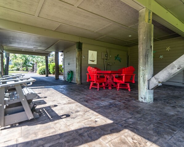 Un espacio al aire libre techado con mesas de picnic y sillas Adirondack rojas, una manguera verde y un mural de una tortuga en la pared.