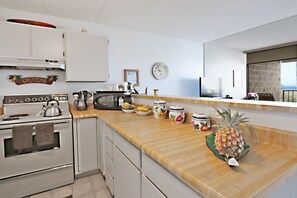 Een moderne keuken met witte kasten, een houten aanrecht, een klok en uitzicht op zee.
