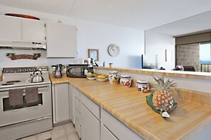 A modern kitchen with white cabinets, a wooden countertop, a clock, and a view of the sea.