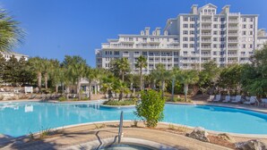 Un complexe hôtelier doté d’une grande piscine, de palmiers et d’un immeuble à plusieurs étages avec des balcons.